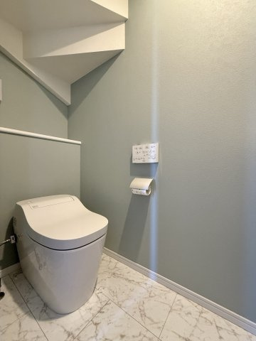 タンクレスで見た目がスッキリとしたトイレです。　背面は収納スペースとなっており、　階段下の空間を無駄なく活用しています。　