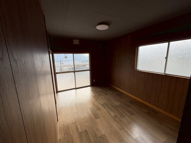 木目調の内装が印象的な落ち着いた洋室です。大きな掃き出し窓からは高台ならではの開放的な眺望が広がり、日中は自然光が室内をやさしく照らします。主寝室としてはもちろん、書斎や趣味部屋としても活用可能です。