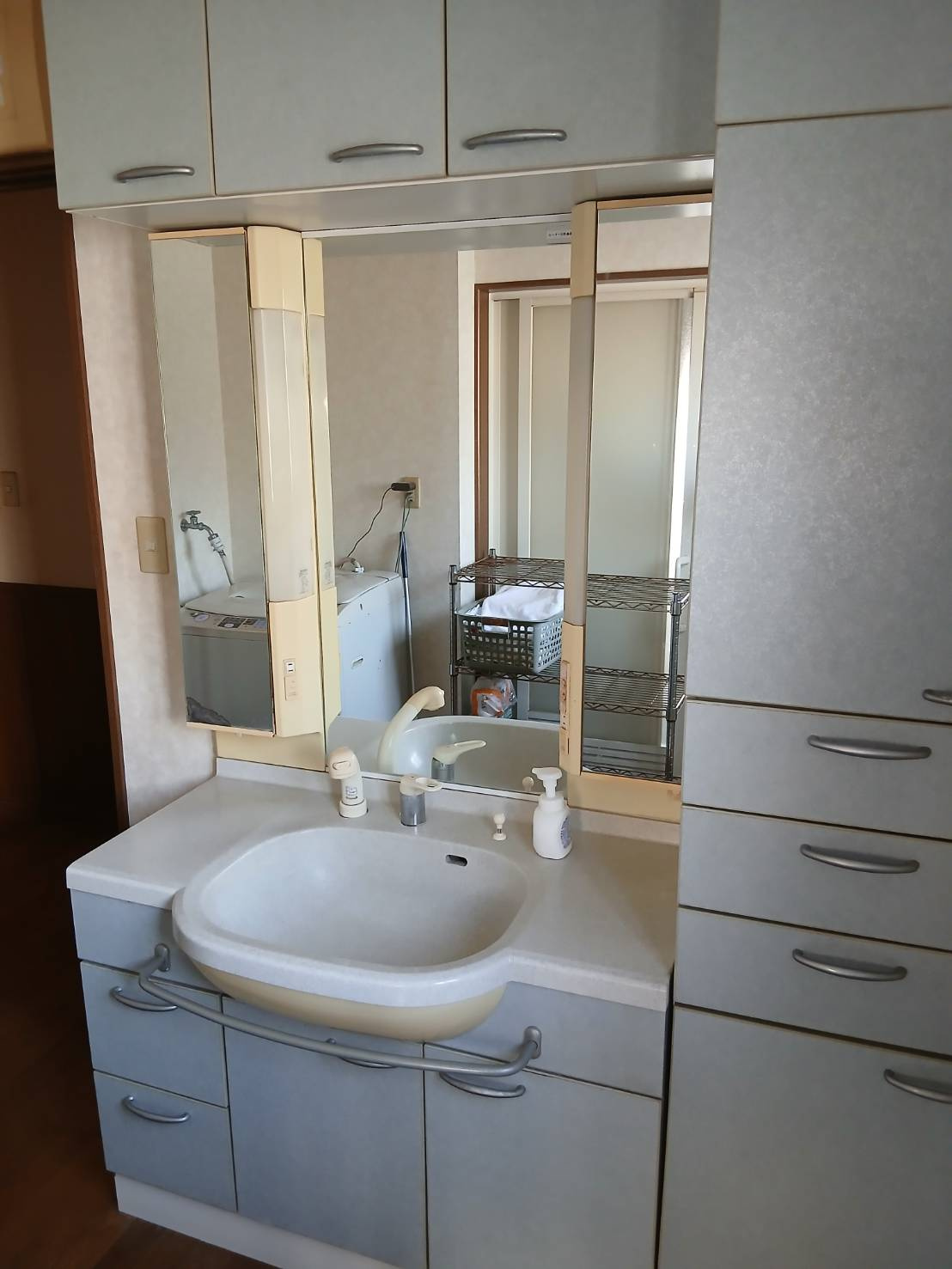 【洗髪洗面化粧台／現地写真】三面鏡タイプ独立洗面台。鏡の裏は収納で、ご家族の皆様で便利に利用可能。