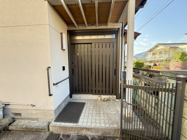 屋根付きの玄関ポーチで雨の日も出入りがしやすく、手すり付きでご高齢の方にも安心の設計です。幅のある引き戸玄関は荷物の持ち運びもスムーズ。落ち着いた色合いの扉で、帰宅時に温かく迎えてくれる雰囲気です。