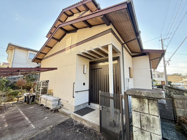 玄関まわりを別角度から見た一枚で、建物の重厚感ある屋根のラインや、奥行きのあるアプローチがよく分かります。屋根の庇がしっかりと確保されており、雨風を防いでくれる安心の設計となっています。