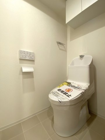 新規交換された清潔感のある温水洗浄便座付きトイレです。衛生的に保ちやすいデザインとなっており、快適にご使用いただけます。上部にはトイレットペーパー等を保管できる便利な収納棚を完備しています。