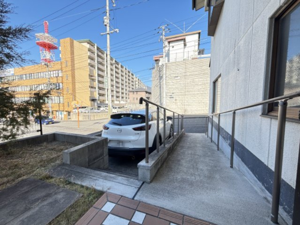 スロープと手すりが設けられ、建物入口まで段差を抑えた動線が確保されています。荷物の搬入出にも便利で、住居兼事務所としての使い勝手を高める駐車スペースです。　