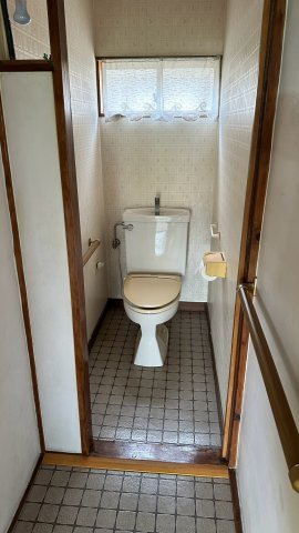 手すりと窓を設置し、手洗い管付きタンクを備えたトイレです。