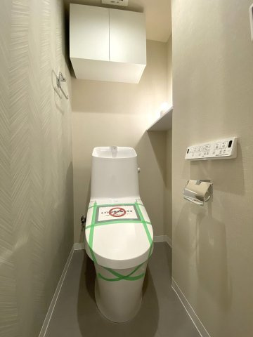 新規交換された清潔感のある温水洗浄便座付きトイレです。衛生的に保ちやすいデザインとなっており、快適にご使用いただけます。上部にはトイレットペーパー等を保管できる便利な収納棚を完備しています。
