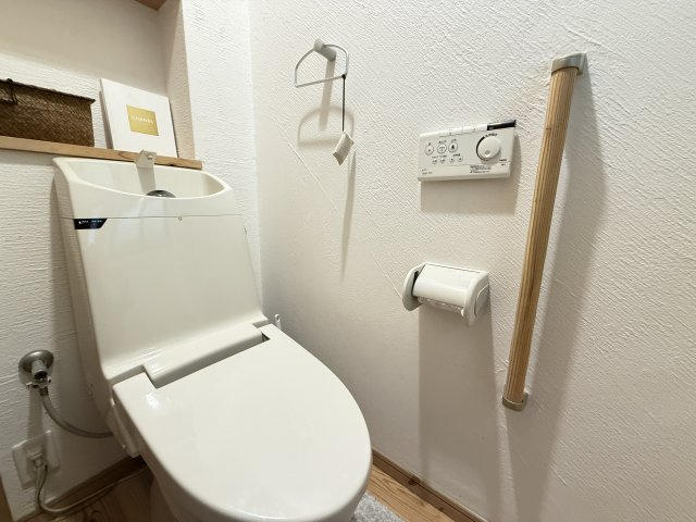 手すり付きで安心設計のトイレ。どなたにも優しい使いやすさが魅力です。温水洗浄便座や操作しやすい壁付けリモコンを備え、機能性も充実。コンパクトながら収納棚もあるため、清潔感を保ちやすいレイアウトです。