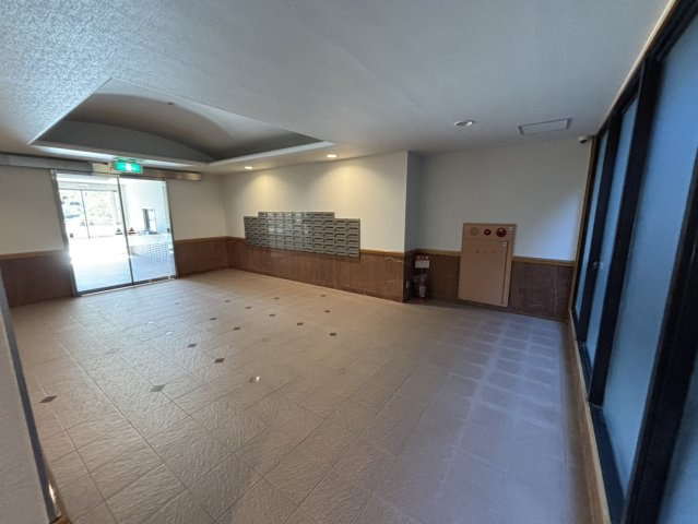 広々としたエントランスホール。落ち着いた色合いのタイル床と木調の壁が上品な印象を与えます。オートロック付きでセキュリティ面も安心です。清掃が行き届いた共用部は、居住者の快適な暮らしを支えています。