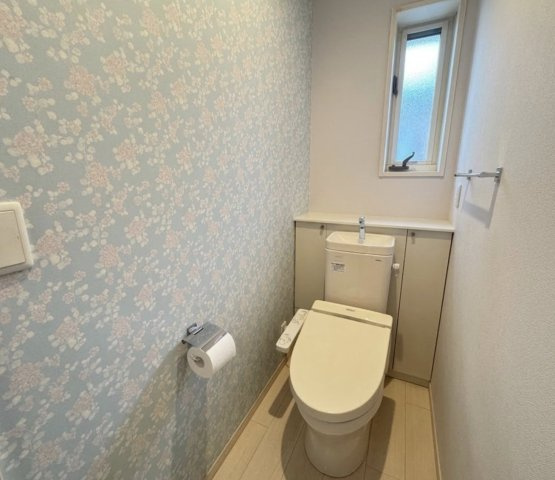 やさしい色合いのアクセントクロスが印象的なトイレ空間。シンプルながらもデザイン性があり、落ち着いて利用できる空間です。収納スペースもあり、トイレットペーパーや備品もすっきり整理できます。