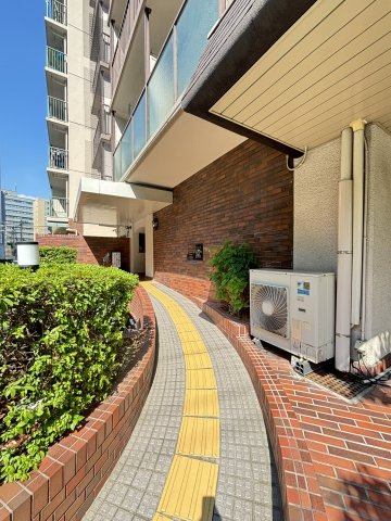 【アプローチ】エントランスへ続くアプローチです。レンガ調の壁面と、黄色い誘導ブロックが設置されたスロープ仕様になっています。