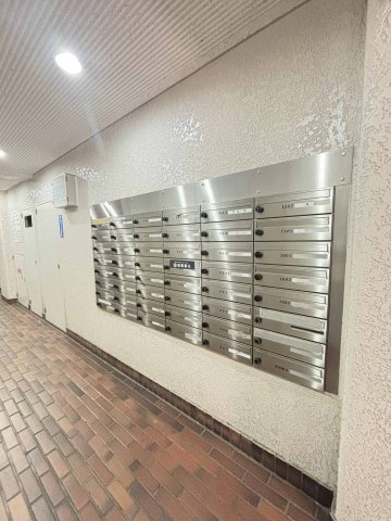 【集合ポスト】一階共用部に設置されたダイヤル式の集合ポストです。ステンレス製のユニットが壁面に並んでいます。