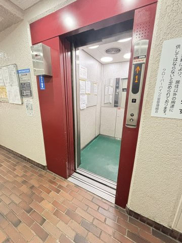 【エレベーター】赤を基調としたフレームが特徴的なエレベーターです。内部には防犯カメラや案内掲示板が設置されています。