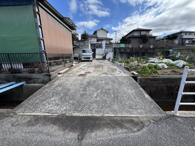敷地へは橋掛け部分を通って進入する形状で、隣地との共有持ち分がございます。道路から一段上がった立地のため、外部からの視線が入りにくく、落ち着いた住環境を確保しやすい点も魅力です。