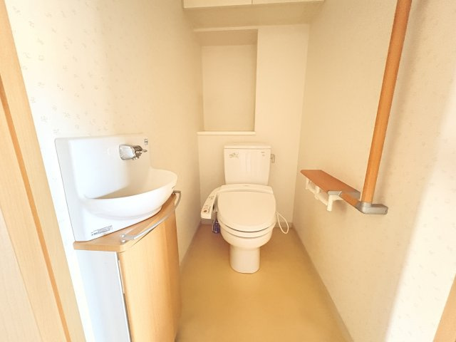 温水洗浄便座付きのトイレは、手洗い器を備えた使い勝手の良い設計です。手すりも設置されており、小さなお子様からご年配の方まで安心してご利用いただけます。上部には収納スペースもあり、備品整理にも便利です。