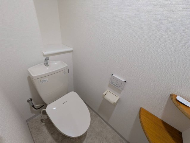 清潔感のあるシンプルなトイレ空間です。温水洗浄便座を備えており、快適にご利用いただけます。手洗い付きタンクを採用しているため、使用後すぐに手を洗うことができ衛生的です。便器奥には棚スペースがあります。