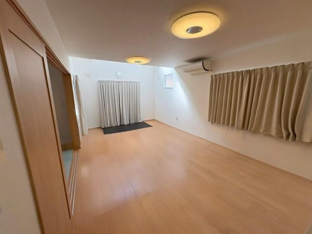 木目調フローリングが温かみを感じさせる広々としたリビングです。吹抜け部分からの採光で、室内全体が明るく開放的な空間です。家具配置もしやすい形状で、家族が自然と集まる団らんの場になります。