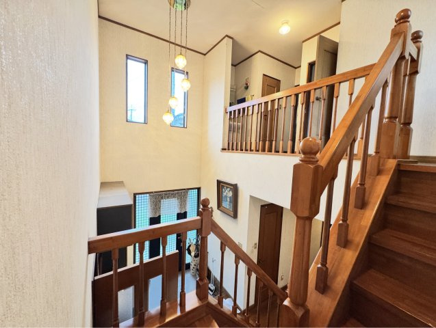 開放感のある吹き抜け階段が印象的な空間。窓から自然光が差し込み、明るく心地よい雰囲気を演出します。手すり付きで安全性にも配慮されており、ご家族皆様が安心してご利用いただける設計となっています。