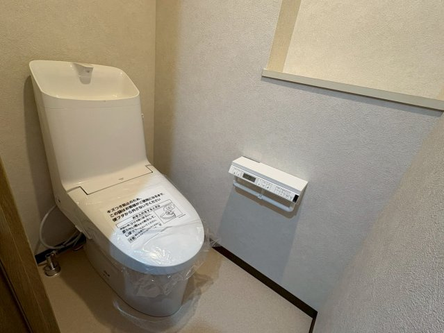 落ち着いた雰囲気のトイレ空間です。温水洗浄便座付きで、快適に使用できます。操作パネルはペーパーホルダーについており、見た目もすっきりします。清潔感があり、毎日気持ちよく使える仕様です。