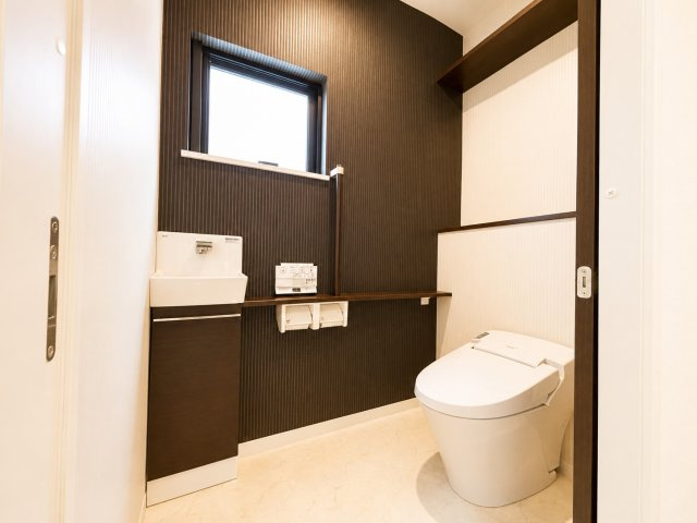 落ち着いた色合いのアクセントクロスが印象的なトイレ空間。手洗いカウンター付きで来客時にも使いやすく収納棚も設けられているため備品類もすっきり整理可能。清潔感と機能性を兼ね備えた空間です。