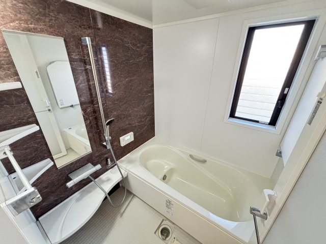 ダークブラウンのアクセントパネルが高級感を演出する浴室。明るい窓付きで換気しやすく清潔な空気を保てます。ゆったり浸かれる浴槽はお仕事終わりの疲れを癒す心地よい空間。手すりや収納棚もあり使い勝手がよい　