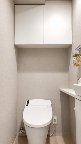 温水洗浄便座付きの清潔感あるトイレ。手洗いカウンターや吊戸棚も備え、収納力と機能性を兼ね備えた快適な空間です。