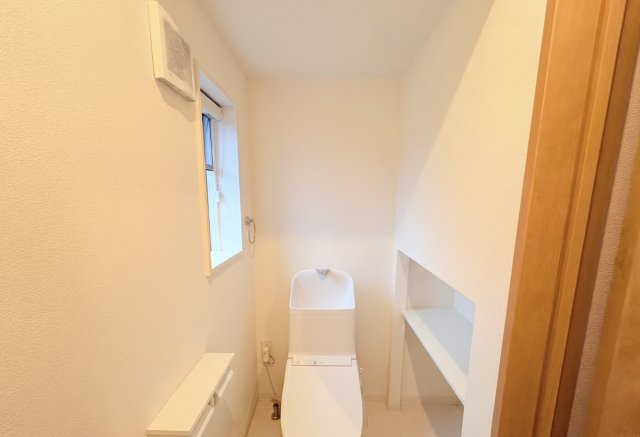 白を基調とした、清潔感あふれるトイレです。窓付きのため換気がしやすく、明るさもしっかり確保されています。温水洗浄便座付きで快適に使用でき、壁面には収納スペースも設けられており、すっきり整理可能です。