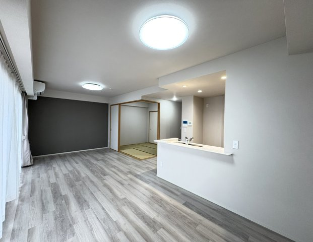 室内全体を見渡しやすい対面式キッチンを採用しており、調理中もリビングで過ごすご家族とのコミュニケーションを取りやすい設計です。グレー系のアクセントクロスと明るいフローリングが落ち着いた雰囲気を演出。