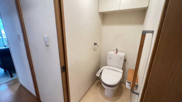 温水洗浄便座を備えた清潔感のあるトイレです。上部には収納棚が設けられており、トイレットペーパーや掃除用品などをすっきり収納可能。手すりも備わっているため、立ち座りの動作にも配慮された使いやすい空間です