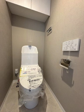 内装や設備を一新した、清潔感あふれるトイレ。本体は新規交換済みの未使用状態で、気持ちよく新生活をスタート可能　。上部には備品をスッキリ収納できる吊戸棚、壁面には操作しやすいリモコンを完備しています　。