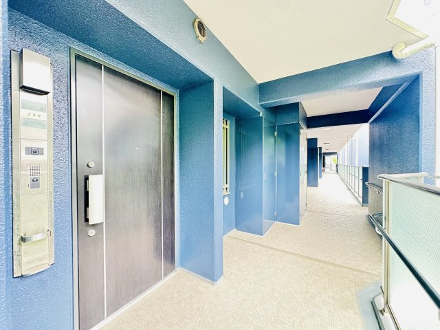 共用廊下に面したスッキリとした玄関アプローチ。　カメラ付きインターホンを備えており来訪者の顔を室内からしっかり確認できるため防犯面でも安心です。　ベビーカー等での出入りもスムーズなフラットな生活動線。