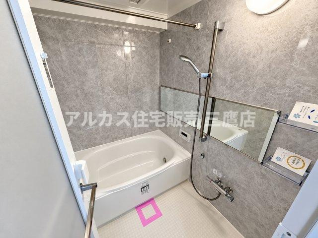 落ち着いた色合いの壁面パネルと清潔感のある浴槽が調和した浴室です。手すりや物干し用のランドリーパイプも設置されています。