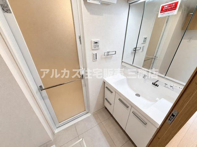 大型の三面鏡とすっきりとした洗面ボウルを備えた洗面化粧台です。左手には浴室へのドアが配置されており、動線がスムーズです。