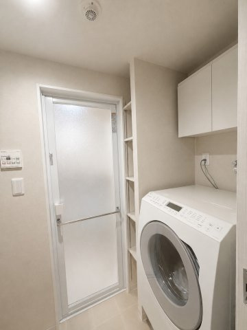 上部に洗濯用品を置ける棚が設置された、使い勝手の良い洗濯機置場。水回りの動線上にすっきりと配置されており、日々の洗濯作業をスムーズかつ効率的にこなせる便利な設計です。