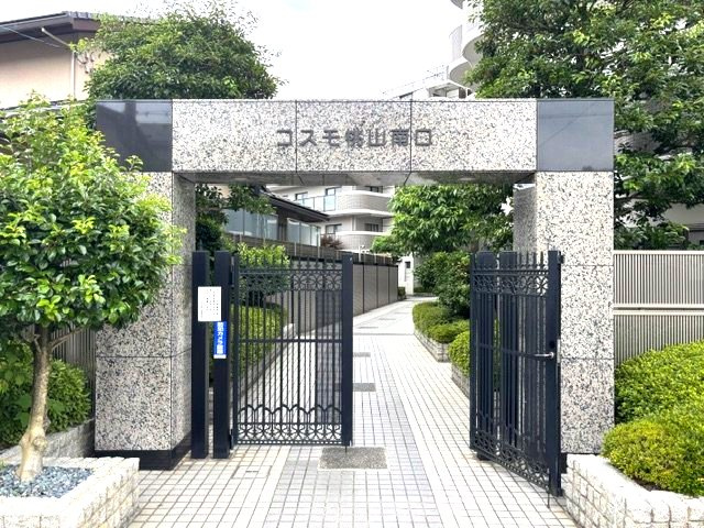 【重厚感のあるマンションエントランス】石造りの立派な門構えとシックな黒い鉄製ゲートが、住まいの格式の高さを演出します。周囲には美しく手入れされた豊かな植栽が広がり、居住者を優しく迎え入れます。