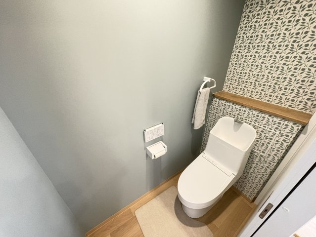 淡い色合いの壁と植物柄のアクセントクロスが印象的な2階トイレです。木目のカウンターも取り入れられ、ナチュラルで落ち着きのある空間に仕上がっています。手洗い一体型で使い勝手にも配慮されています。
