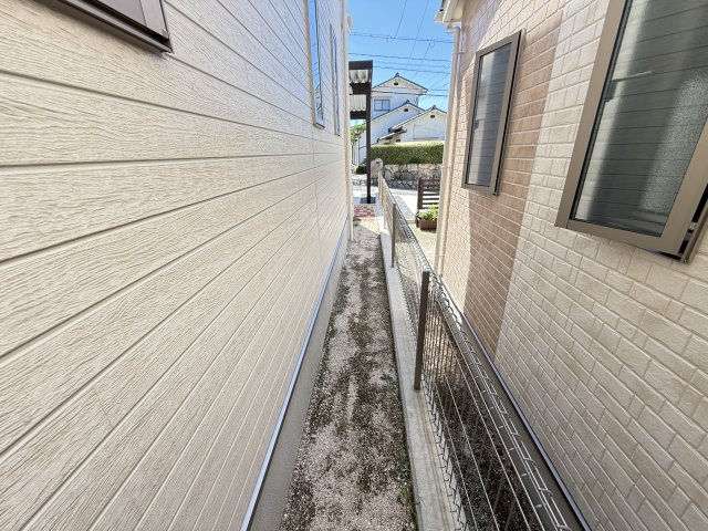 建物周辺はしっかりとしたフェンスで区切られ、安心感のある造りとなっています。通路は風通しが良く、窓からの採光や換気にも役立ちます。お手入れがしやすいシンプルなスペースで、快適な住環境をサポートします。
