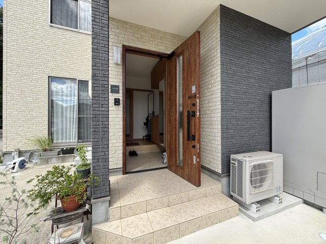 木目調の玄関ドアが温かみを感じさせる、デザイン性の高い玄関まわりです。ゆとりあるポーチで出入りも安心。鉢植えを飾れるスペースもあり、季節の彩りを楽しみながら来客を迎えられる心地よいアプローチです。
