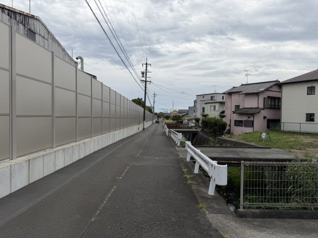 現地から続く前面道路の様子。周辺には住宅や建物が建ち並び、街の雰囲気を確認できます。