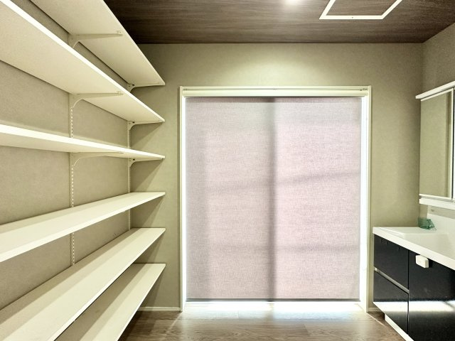 可動式の棚が壁一面に設けられた収納力大のスペースは、日用品やタオル、洗剤類のストックに最適。すぐ隣には洗面台もあり、動線が非常に効率的です。スッキリとした空間を保てる理想的な設計です。