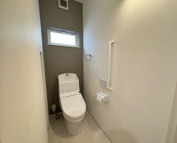 シンプルで清潔感のあるトイレ空間。温水洗浄便座付きで快適にご利用いただけます。手すりも設置されており小さなお子様やご年配の方にも安心の設計。窓付きで自然換気が可能なため、いつでも気持ちよく使える空間。