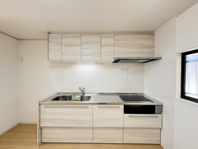 木目調の扉が室内のフローリングと調和した、すっきりとしたデザインのシステムキッチン。上下に収納スペースが設けられており、調理器具や食器、ストック品などを整理しやすい仕様。作業スペースもしっかり確保。