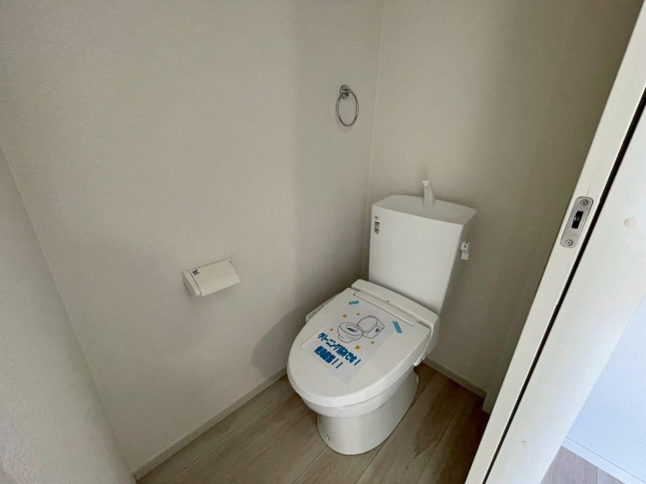 白を基調とした清潔感のあるトイレ空間です。温水洗浄便座を標準装備しており、快適にご使用いただけます。ペーパーホルダーやタオルリングも設置済みで、シンプルながら使い勝手の良い設計です。