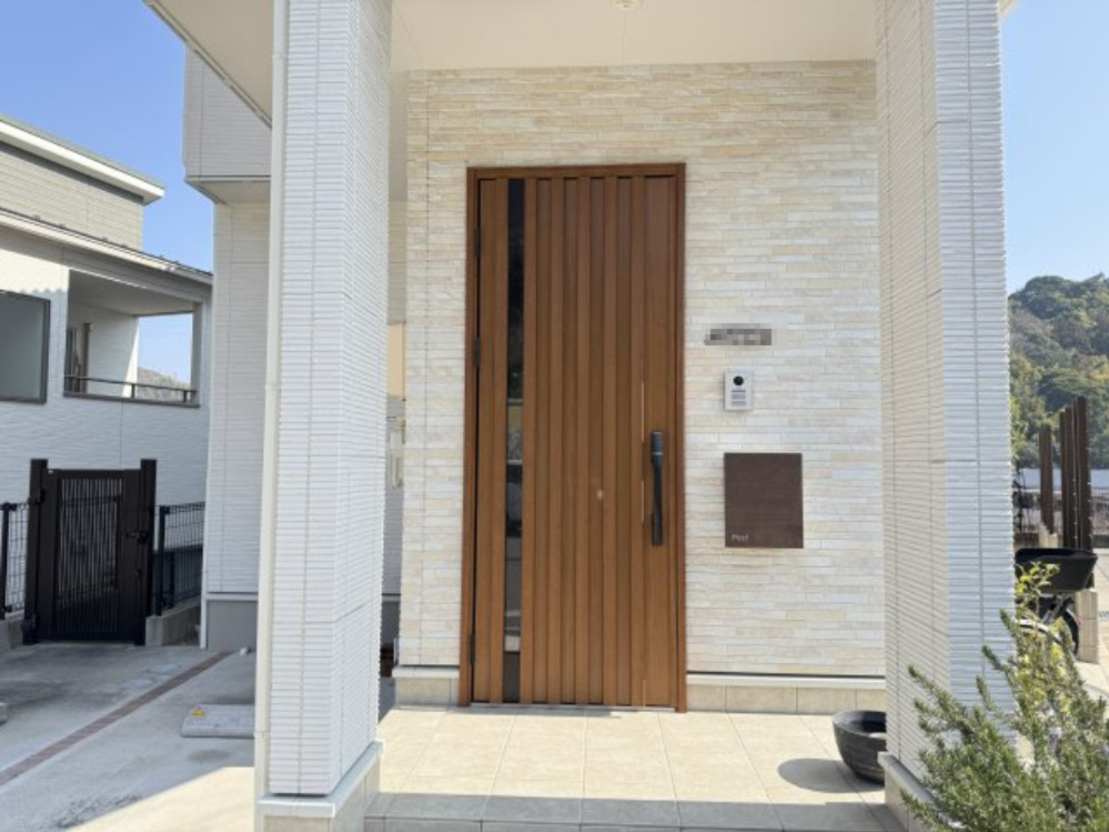 縦格子デザインの木目調ドアが印象的な玄関アプローチ。明るい外壁とのコントラストが美しく上質で落ち着いた雰囲気を演出します。ポーチには屋根があり雨の日でも安心。インターホンやポストもすっきりと配置
