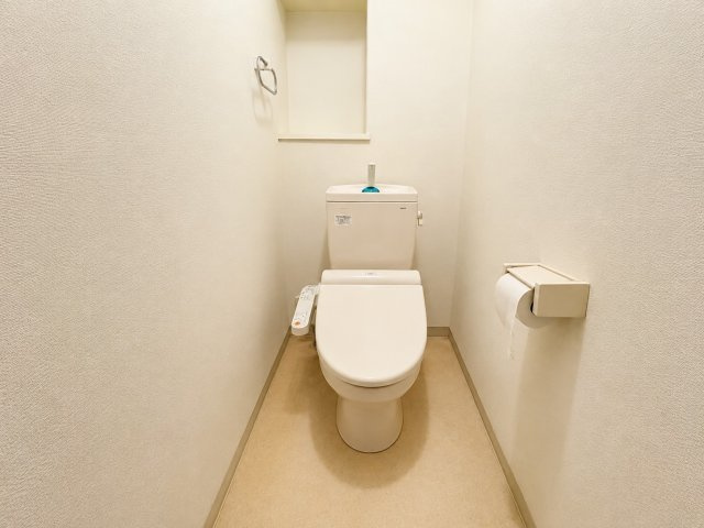 白を基調とした、明るく清潔感のあるトイレです。温水洗浄便座を備え、毎日快適にお使いいただけます。手洗い付きのタンクやタオルリング、ペーパーホルダーも設置されており、必要な設備がすっきりとまとまった空間