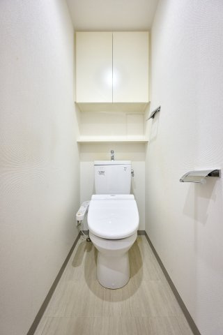 白を基調とした清潔感と落ち着きのあるトイレ空間。温水洗浄便座を標準装備し、上部にはトイレットペーパーや備品をスマートに収納できる便利な棚が設置されています。
