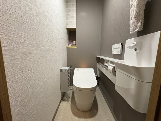 落ち着いた内装のトイレ空間。手洗いカウンター付きで、来客時にも使いやすい仕様です。上部や背面に収納スペースがあり、トイレットペーパーや掃除用品を隠して収納可能です。清潔感と機能性を兼ね備えています。