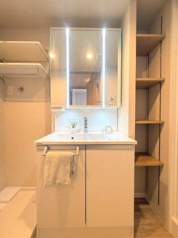 ライト付きミラーで使いやすい洗面化粧台。三面鏡タイプで、角度を変えて細部までチェックできる快適な使い心地。　鏡裏にはたっぷりの収納スペースを確保し、化粧品や洗面用品もすっきり整理。サイドに収納棚も完備
