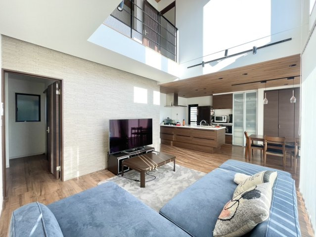 吹き抜けの大きな窓から自然光が降り注ぐ明るいリビング。視線が上へ抜けるため実際の帖数以上に広さを感じられます。2階ホールのアイアン手すりがアクセントとなり、デザイン性も高い空間に。