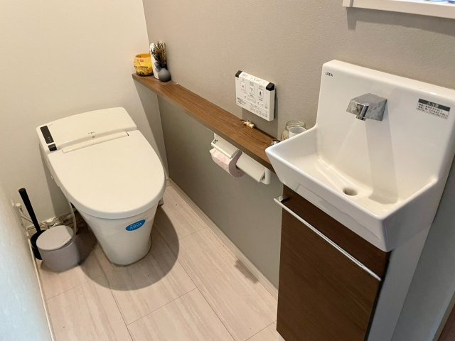 落ち着いた色合いでまとめられた清潔感あるトイレ空間。手洗い器付きで衛生面にも優れ、来客時にも使いやすい仕様。奥行きあるカウンターは小物のディスプレイやストック収納にも便利。温水洗浄便座や節水タイプ！
