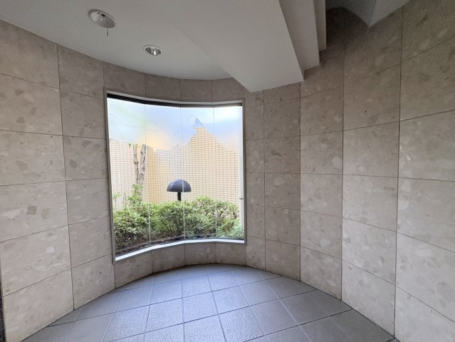 石調の壁面と曲線を取り入れたデザインが印象的な共用スペースです。大きな窓の向こうには植栽が配置され、建物内にいながら自然の緑を感じられる落ち着いた雰囲気。シンプルながら上品さを感じさせる内装です。