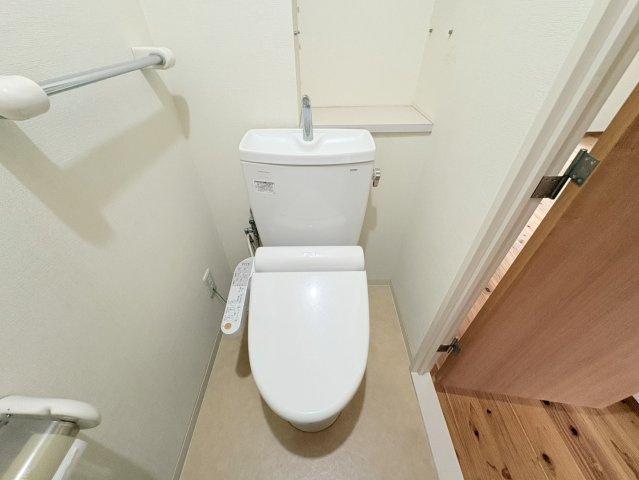白を基調とした清潔感のあるトイレです。手洗い付きの便器を採用し、壁面にはタオル掛けや棚も設けられています。すっきりとした内装で圧迫感を抑え、毎日気持ちよく利用できるシンプルで使いやすい空間です。